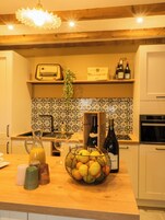 Una cocina con mostrador de madera, una botella de vino, un frutero y un radio.