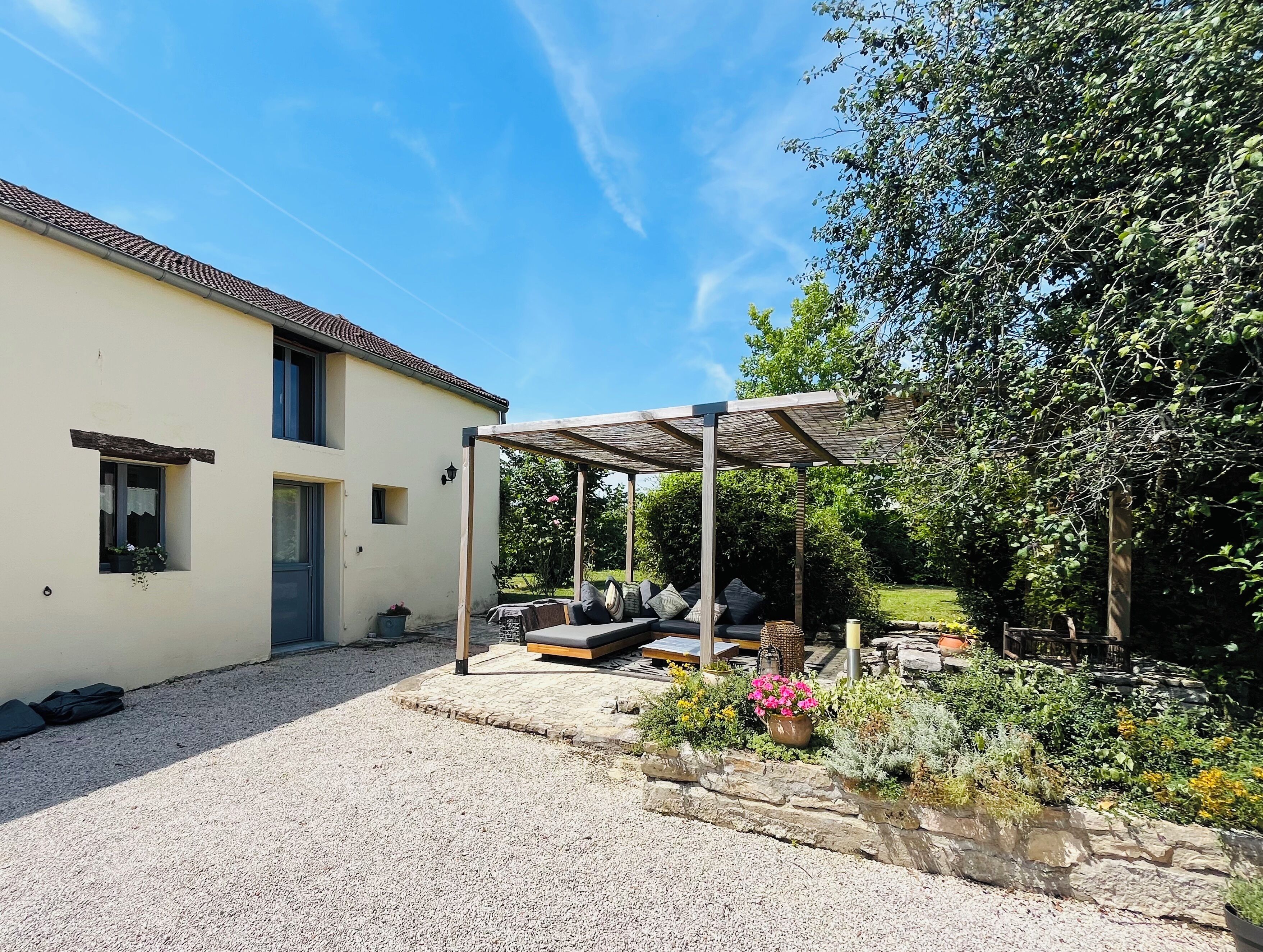 A house with a covered patio, a gravel driveway, and a garden with various plants and flowers.