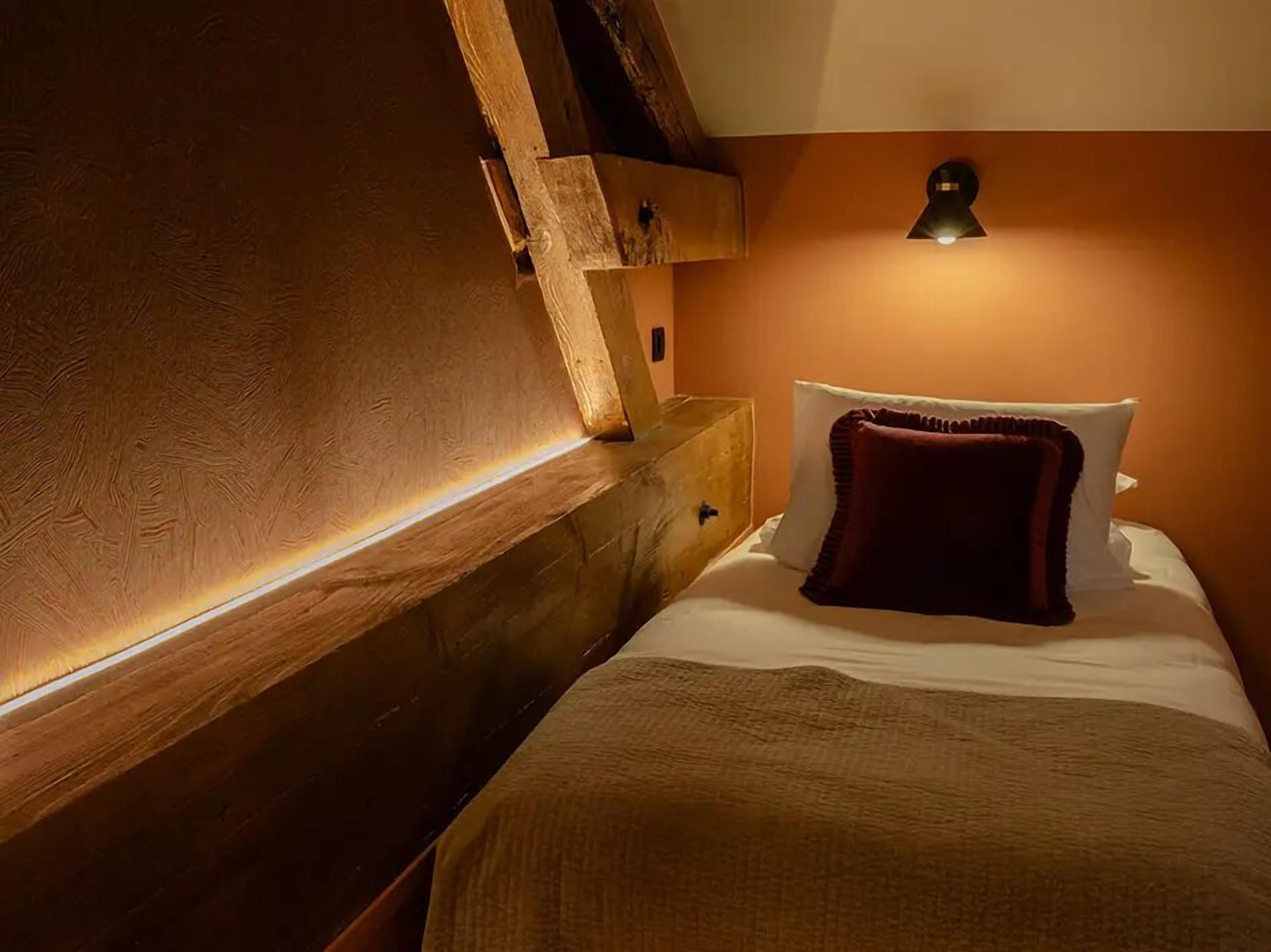 Ein gemütliches Zimmer mit einem hölzernen Kopfteil, einem Einzelbett mit roter Decke und einer Wandleuchte.