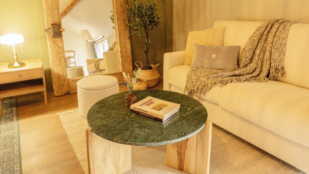 Een gezellige woonkamer met een ronde houten salontafel, een witte bank met een plaid en een spiegel met houten lijst.