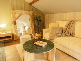 Un salón acogedor con una mesa redonda de madera, un sofá blanco con una manta y un espejo con marco de madera.