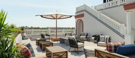 A rooftop terrace with outdoor seating, including sofas and tables, and a staircase leading to an upper level.