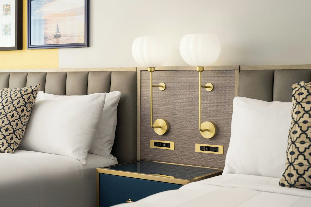 A hotel room with a bed, a nightstand, and a wall-mounted lamp.