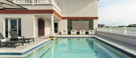 A modern pool area with a clear pool, lounge chairs, and a white fence.