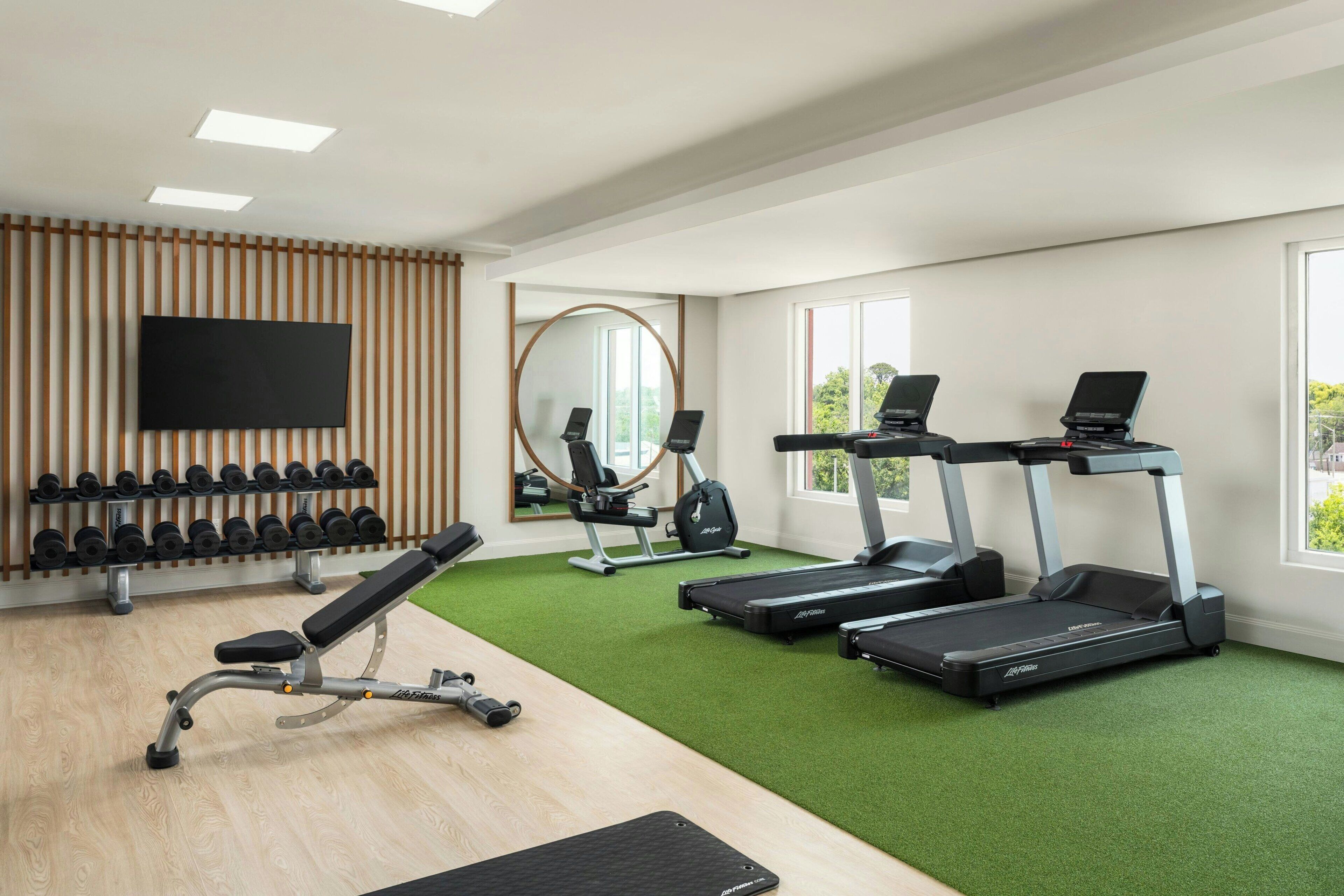 Ein modernes Fitnessstudio mit Laufbändern, einer Bank, Kurzhanteln und einem Spiegel.