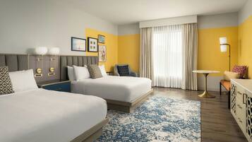 A hotel room with two beds, a desk, a chair, a small table, and a lamp.