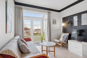Una sala de estar moderna con un sofá, una mesita, una silla, un televisor y un balcón con vistas a edificios.