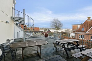 A wooden deck with outdoor seating, a spiral staircase, and a view of the surrounding neighborhood.