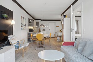 Una sala de estar moderna con sofá, mesa de comedor, sillas y una cocina con armarios y una lámpara colgante.