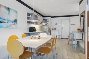 A modern kitchen with white cabinets, a dining table with yellow chairs, and pendant lighting.