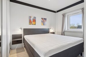 A bedroom with a bed, two wall-mounted light fixtures, a window with curtains, and two abstract paintings on the wall.