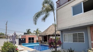 A swimming pool surrounded by lounge chairs and a palm tree, with a building in the background. - Puerto Vallarta Calm Getaway with Pool  (Puerto Vallarta)