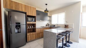 A modern kitchen with a built-in refrigerator, microwave, and coffee maker. There is a bar area with stools and a window providing natural light. - Puerto Vallarta Calm Getaway with Pool  (Puerto Vallarta)