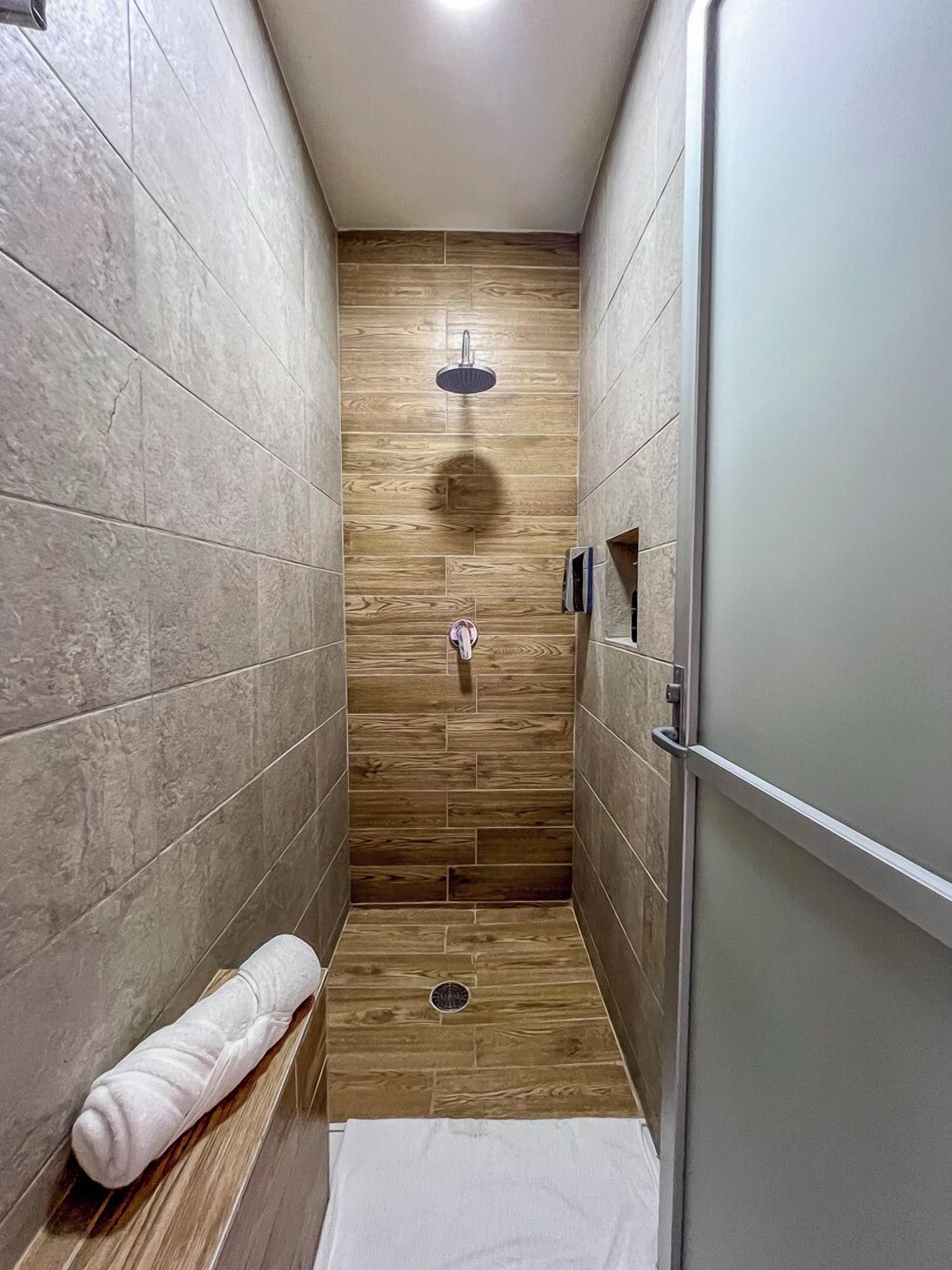 A narrow shower area with wooden flooring, a towel on the floor, and a showerhead.