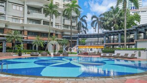 A swimming pool with a blue and white mosaic design, surrounded by palm trees and a multi-story building with balconies. - Camila by Kozystay - Kuningan (Jakarta)