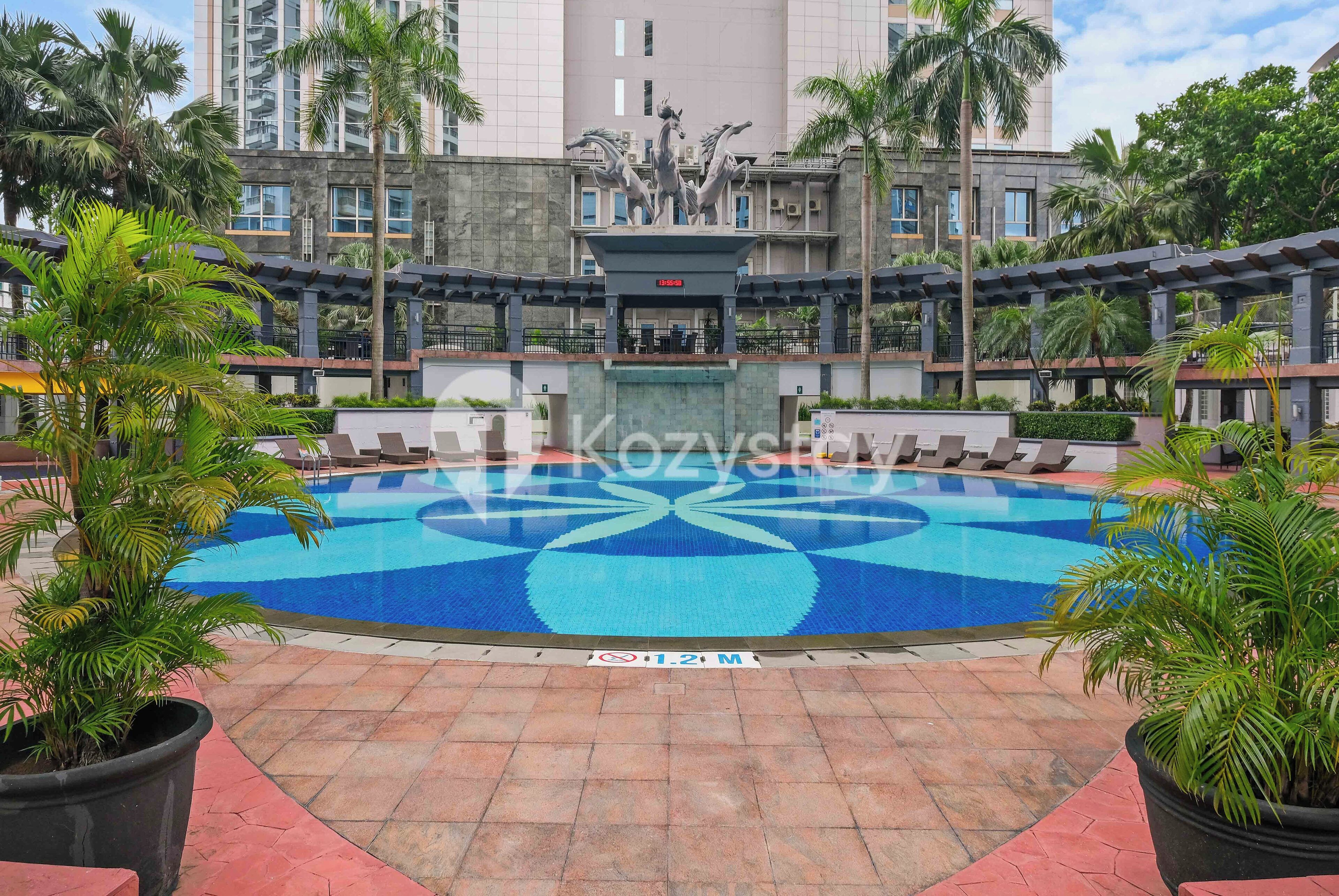 A swimming pool with a decorative fountain in the center, surrounded by palm trees and lounge chairs.