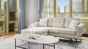 A modern living room with a beige sectional sofa, a white coffee table, and a large window offering a city view. - Camila by Kozystay - Kuningan (Jakarta)