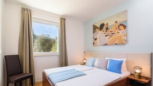 Un dormitorio con una cama grande, una silla, una mesita de noche con lámpara y un cuadro en la pared.