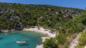 Una playa con agua turquesa cristalina, un bote y una ladera rocosa.
