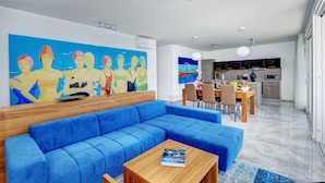 Una sala de estar moderna con un sofá azul, una mesa de centro de madera y un cuadro abstracto y colorido en la pared.