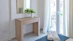 A bedroom with a wooden bedside table, a vase with flowers, a blue bedspread, and two rolled towels on the bed. - Zografia Apartments (Corfu)