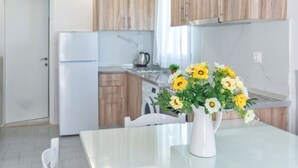 A modern kitchen with wooden cabinets, a white refrigerator, and a dining table with a vase of flowers. - Zografia Apartments (Corfu)