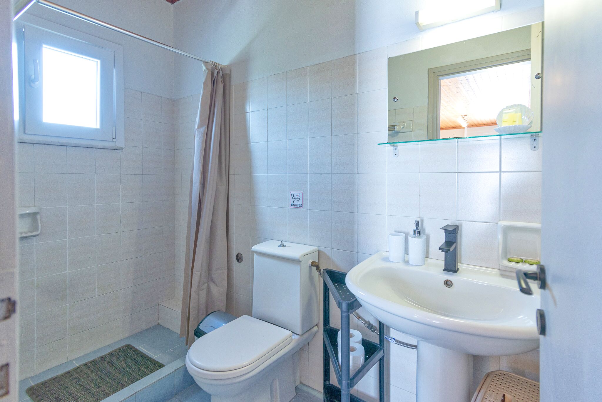 A bathroom with a toilet, shower, sink, and a window.