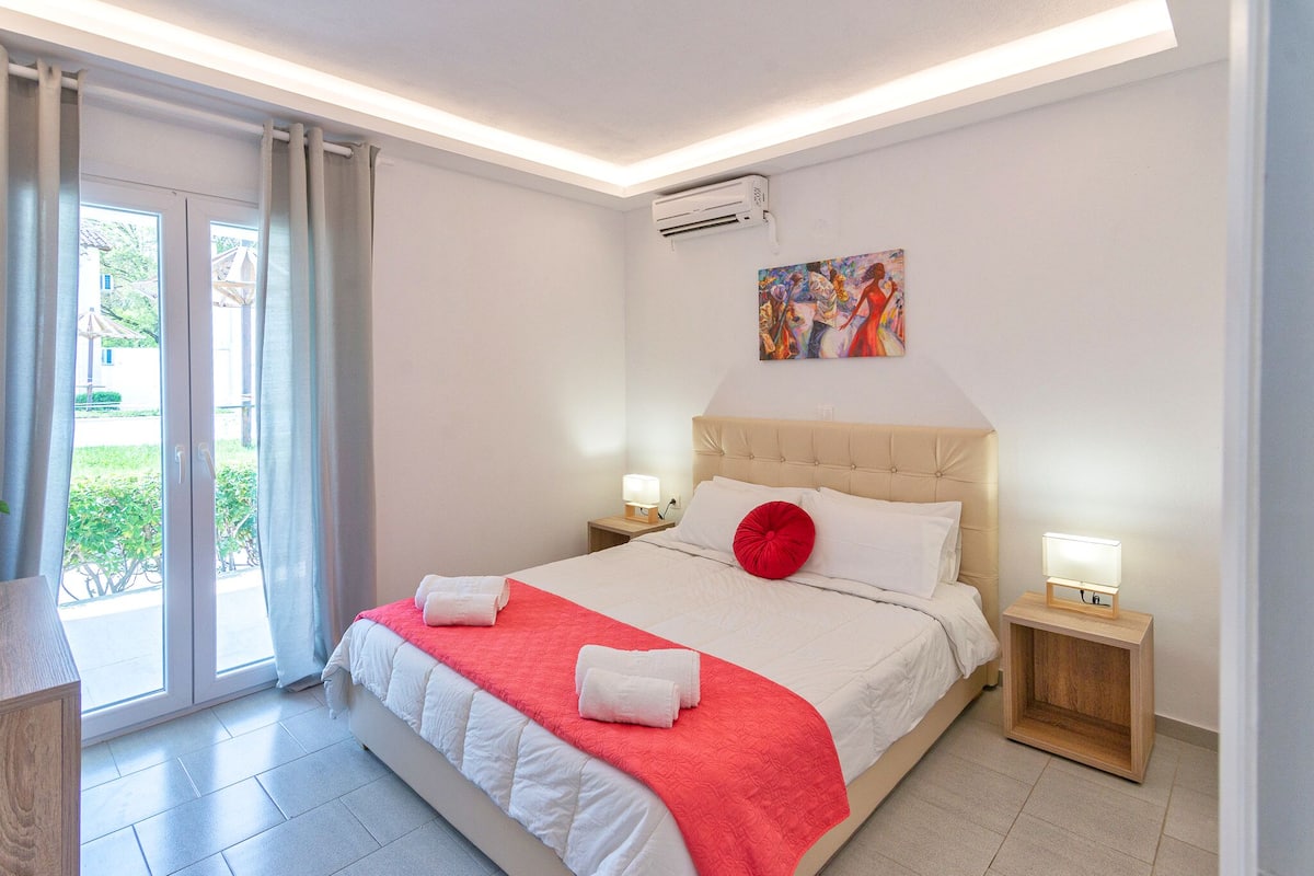 A bedroom with a bed, a nightstand, a painting, and a sliding glass door to the outside.
