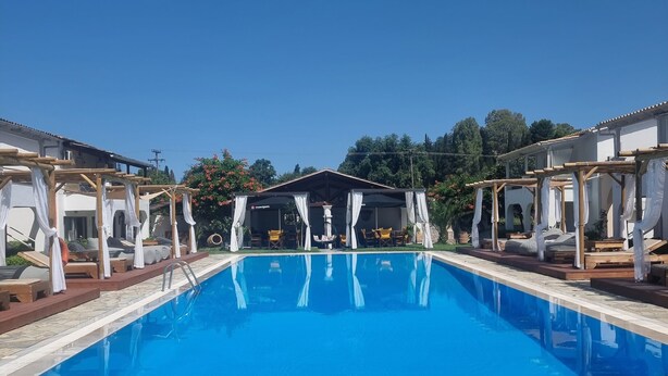 A swimming pool with a stone deck, surrounded by wooden pergolas with white curtains. - Zografia Apartments (Corfu)