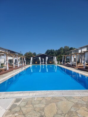 A swimming pool with a stone deck, surrounded by wooden pergolas with white curtains.
