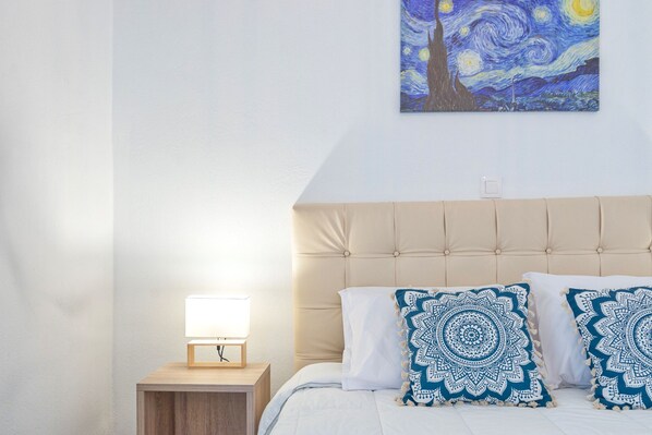 A bedroom with a bed, nightstand, lamp, and a painting of a night sky.