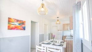 A bright dining area with a white table, two chairs, and a colorful abstract painting on the wall. - Zografia Apartments (Corfu)