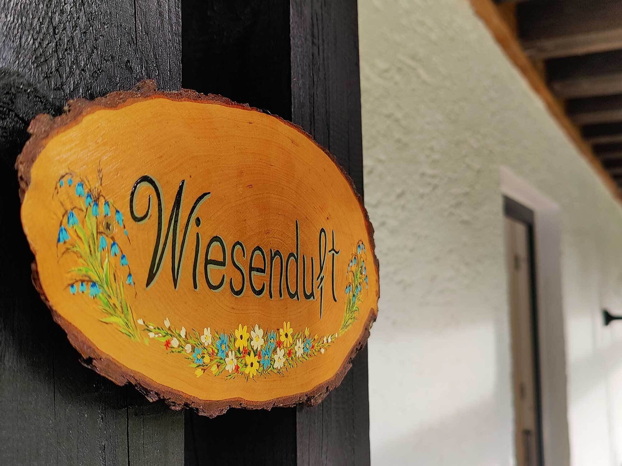 En träskylt med namnet ”Wiesendorf” och blomsterdekorationer.
