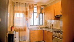 A compact kitchen with wooden cabinets, a gas stove, and a sink. - Wins Homes (Kigali)