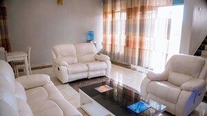 A living room with a white leather sofa, a coffee table, and a water dispenser. - Wins Homes (Kigali)