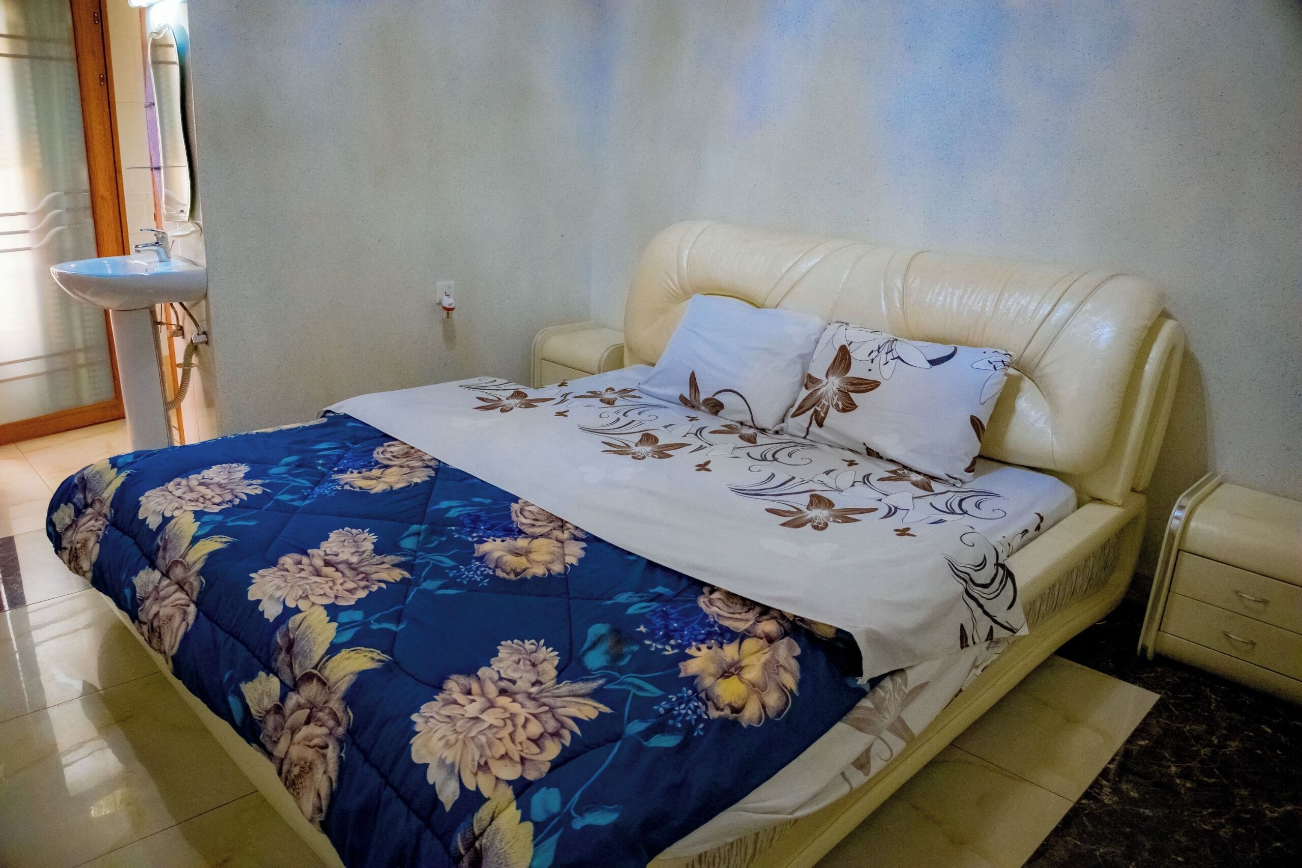 A bedroom with a bed, a nightstand, a bedside table, and a bathroom with a sink.