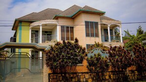 A two-story house with a balcony, a stone wall, and a metal gate. - Wins Homes (Kigali)