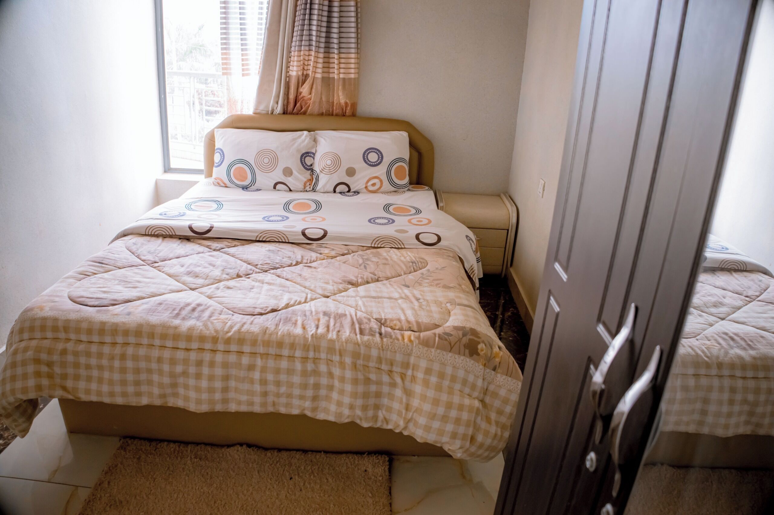 A neatly made bed with a checkered duvet, a bedside table, and a wardrobe.