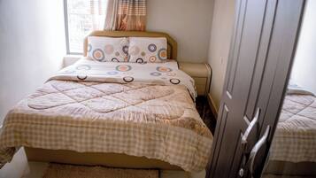 A neatly made bed with a checkered duvet, a bedside table, and a wardrobe.