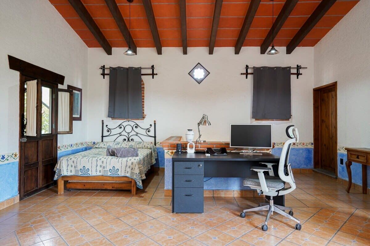 A bedroom with a bed, desk, chair, and a TV.