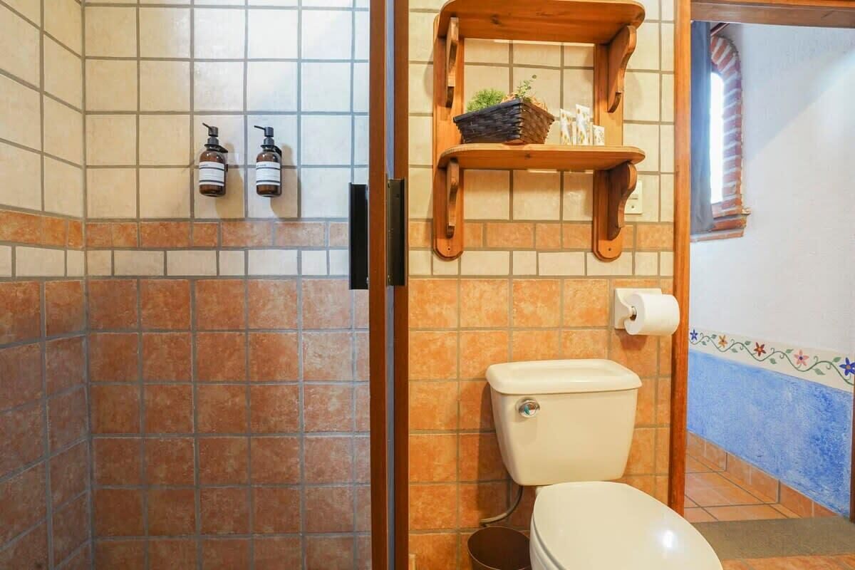 A bathroom with a toilet, a shower area, and a shelf with toiletries.