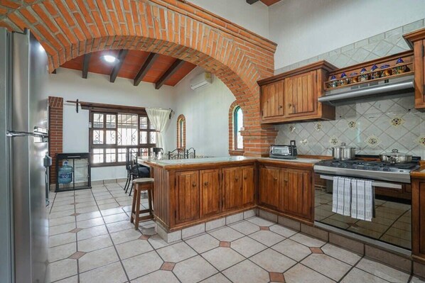 A kitchen with wooden cabinets, a tiled backsplash, and a brick archway. - Family house in Oaxtepec Pool & Hot tub (Yautepec)