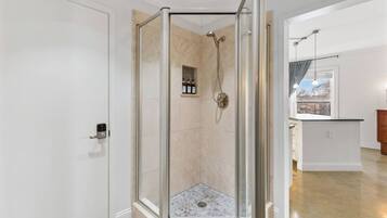 Et moderne badeværelse med et glasafskærmet brusebad, en lille hylde med toiletartikler og udsigt udad gennem et vindue.