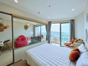 A hotel room with a large bed, a mirror, a view of the city, and a balcony with chairs. - The Sóng Apartment – Near the beach (Ho Chi Minh City)