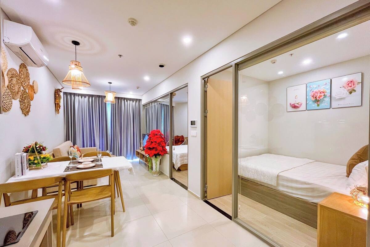 A modern hotel room with a dining area, a bed with a wooden headboard, and a glass partition.