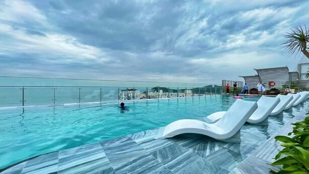 Una piscina a sfioro sul tetto con vista aperta sull'oceano, sedie a sdraio bianche e un edificio moderno sullo sfondo.