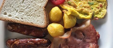 A plate with toast, eggs, sausages, potatoes, bacon, and a tomato slice.