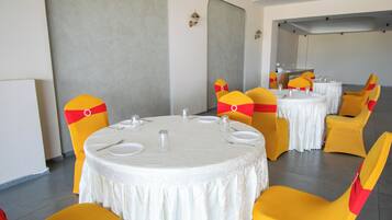 Un salón de conferencias con mesas redondas, sillas amarillas con cintas rojas, manteles blancos y vasos pequeños.