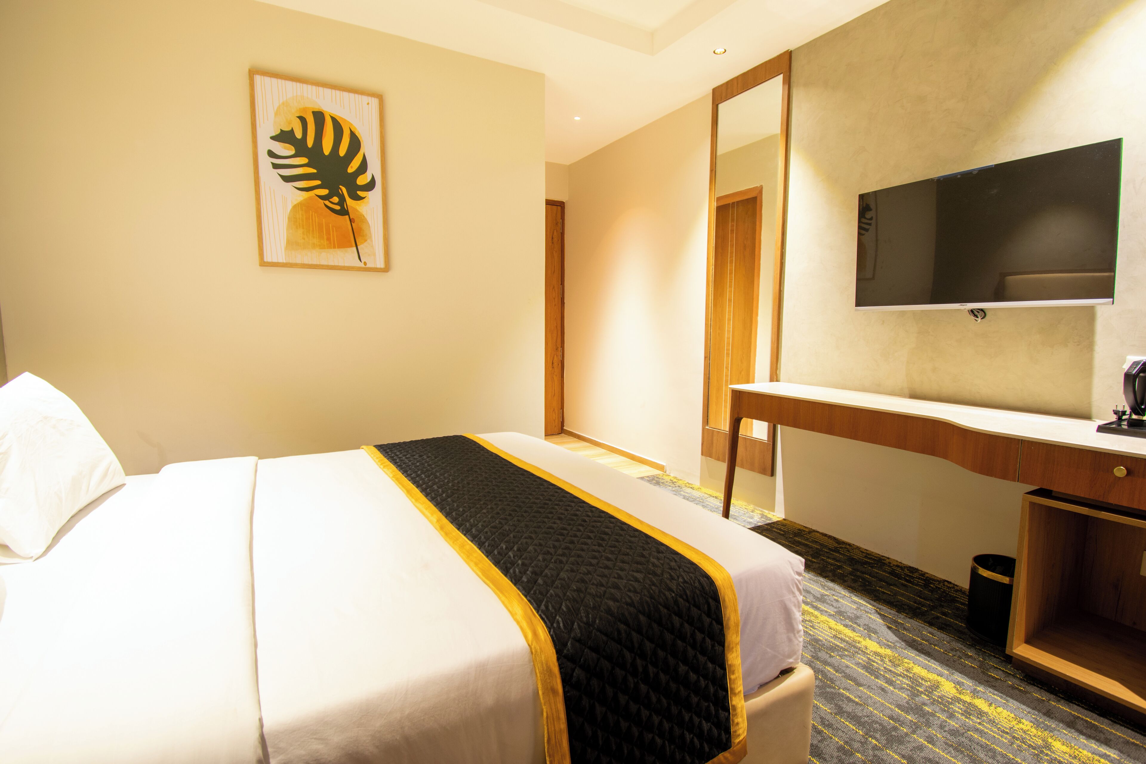 A hotel room with a bed, a desk, a television, and a painting on the wall.