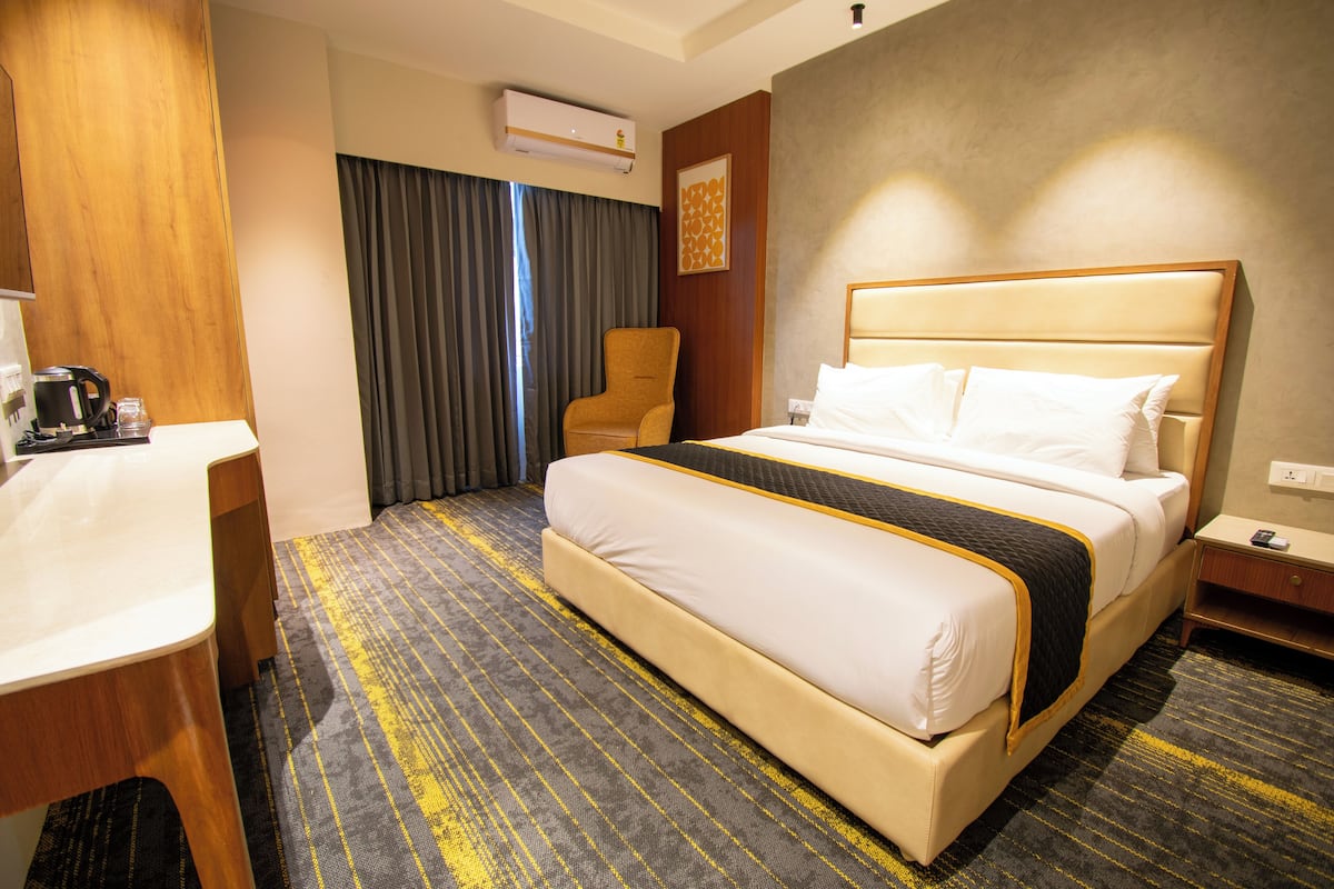 A hotel room with a bed, a desk, a chair, an air conditioning unit, and a wall-mounted artwork.